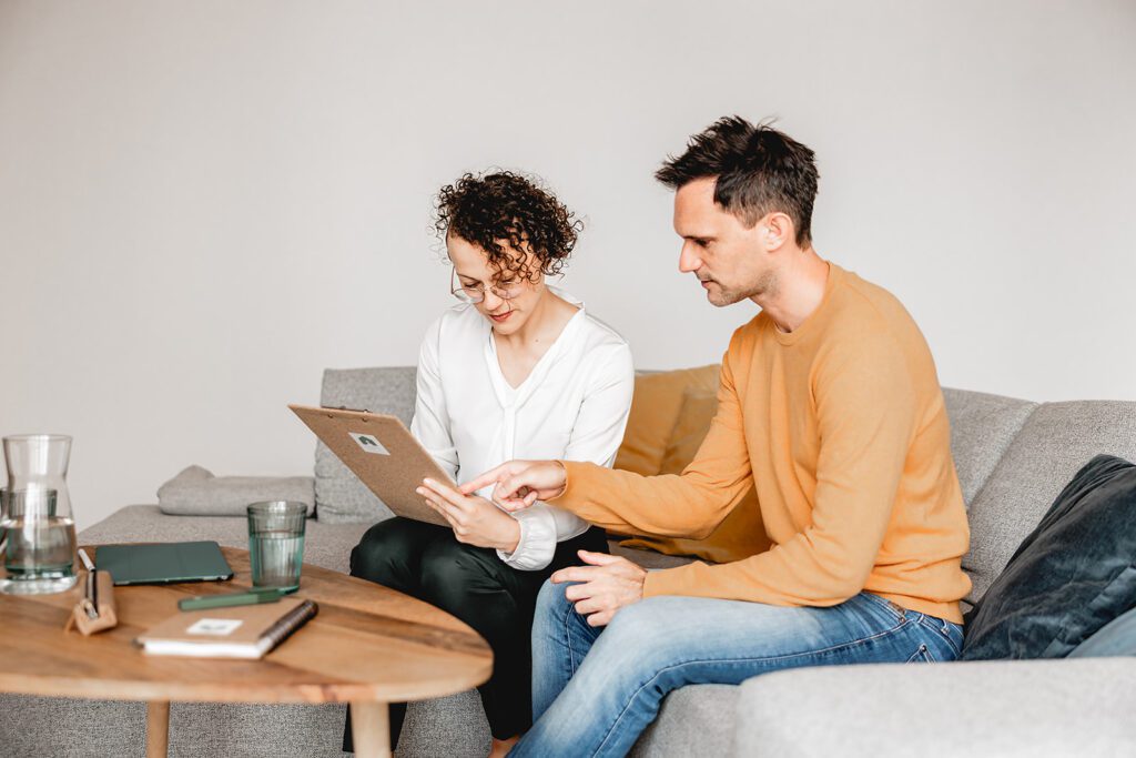 Katja Kammerer und ihr Kunde prüfen gemeinsam eine Checkliste zur Bedarfsanalyse im Beratungsgespräch als Vorbereitung zum Immobilienkauf.