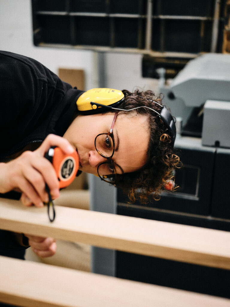 Katja Kammerer misst die Stärke einer Holzlatte, die sie zuvor gehobelt hat.