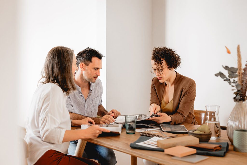 Immobilienberaterin und Kunde besprechen am Tisch anhand von Plänen und Materialmustern individuelle Gestaltungs- und Raumkonzepte für eine Immobilie.