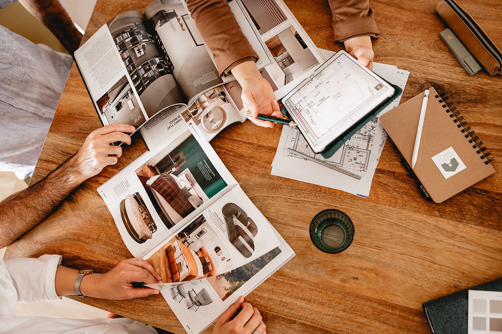 Drei Personen in einem Beratugsgespräch diskutieren am Tisch mit Wohnzeitschriften und Grundrissen über Gestaltung ihrer neuen Wohnung.