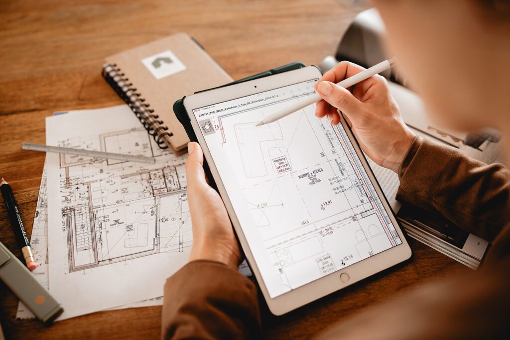 Katja Kammerer prüft bei der Immobilienkauf-Beratung digitale und gedruckte Baupläne am Schreibtisch. Sie bietet auch technische Beratung für Immobilienmakler an.